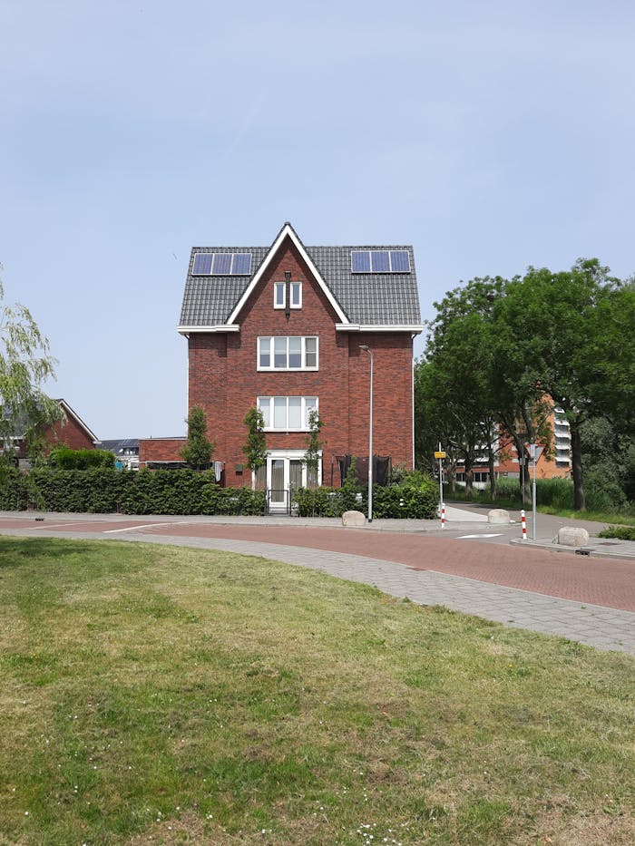 Brick house with solar panels, surrounded by greenery, under a clear blue sky.